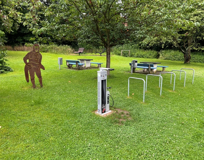 Rastplatz Petershagen  Rastplatz mit überdachten Picknicktischen, Spielskulptur, Fahrradständern und grüner Umgebung in Petershagen.