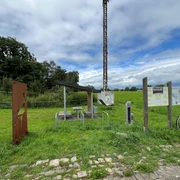 Rastplatz Windheim  Rastplatz mit Tisch und Bänken unter einem Dach, umgeben von grünen Wiesen und Informationstafeln.