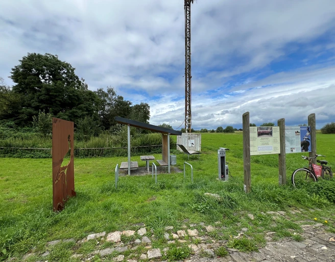 Rastplatz Windheim  Rastplatz mit Tisch und Bänken unter einem Dach, umgeben von grünen Wiesen und Informationstafeln.