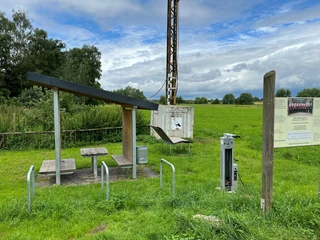 Rastplatz Windheim  Rastplatz mit Überdachung und Picknicktisch inmitten einer grünen Wiese unter bewölktem Himmel.