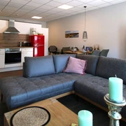 FeWo thelivingroom-wohnbereich.jpg Moderner Wohnbereich mit offener Küche, gemütlicher Couch und stilvollen Dekorationselementen im Raum.