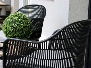 FeWo-thelivingroom-terrasse-außenbereich.jpg Zwei schwarze Rattansessel mit grauen Polstern und einer Dekokugel auf einer Terrasse.