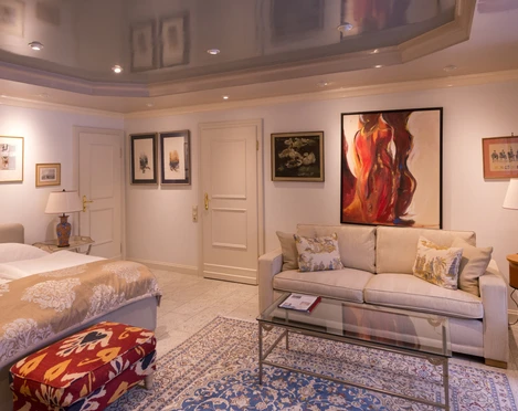 Zimmer in der Villa Mettmann Helles Zimmer in der Villa Mettmann mit Doppelbett, Sofa, Glastisch und Kunstwerken an den Wänden.