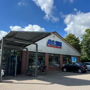 ALDI.jpg Ein ALDI-Supermarkt mit Backsteinfassade. Vor dem Gebäude stehen mehrere Autos. Der Himmel ist blau mit Wolken.