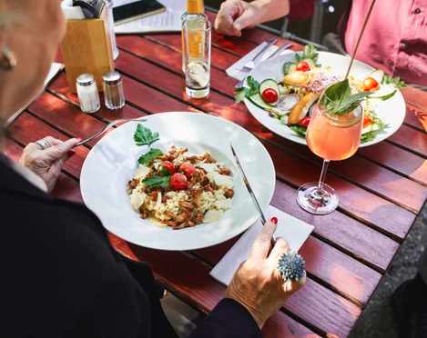 Stadtgarten Eine stilvolle Tischszene im Freien. Im Vordergrund ein Teller mit Pasta garnierte Kirschtomaten und Kräutern.A stylish outdoor table setting. In the foreground, a plate of pasta garnished with cherry tomatoes and herbs.