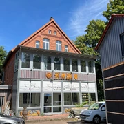 KreativWerkstatt am Wall Ein Backsteingebäude mit großen Fenstern und verzierten Holzdetails bei sonnigem Wetter.