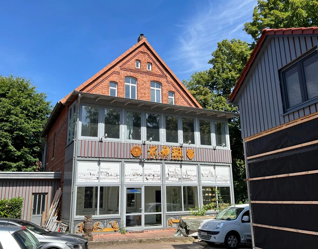 KreativWerkstatt am Wall Ein Backsteingebäude mit großen Fenstern und verzierten Holzdetails bei sonnigem Wetter.