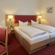 Doppelzimmer im Hotel zur Traube in Velbert Helles Doppelzimmer mit zwei Einzelbetten, rotem Teppichboden, Schreibtisch und einer roten Rose.
