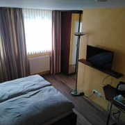 Doppelzimmer in der Krone Homberg in Ratingen Ein Doppelzimmer in Ratingen mit Doppelbett, Holzboden, Fernseher, Tisch mit Wasserkocher und Vorhängen.