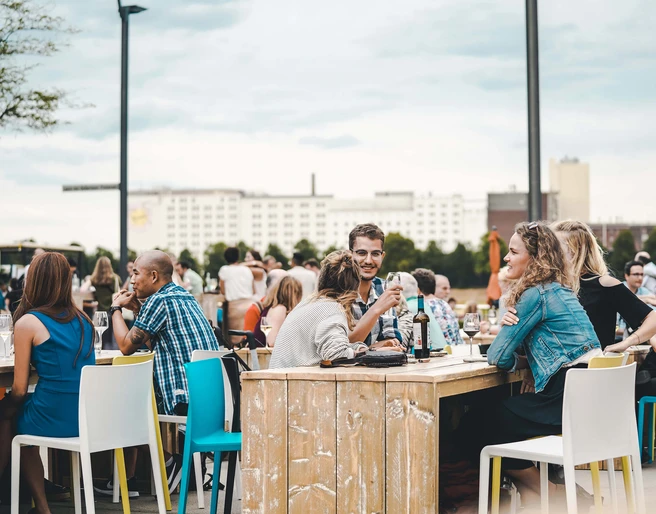Wine festival on the Rhine Menschen sitzen an Holztischen im Freien, genießen Getränke, vor einer urbanen Kulisse.People sit at wooden tables outdoors, enjoying drinks, against an urban backdrop.
