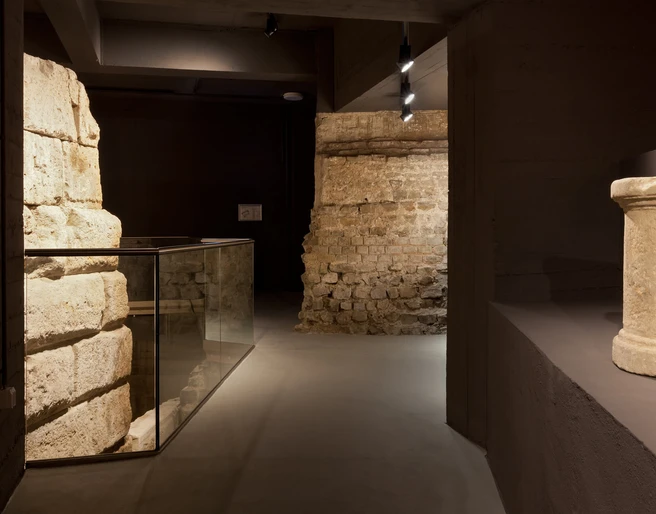 Ubiermonument Im Bild sind historische Mauerwerke aus dem antiken Ubiermonument in Köln zu sehen. Im Vordergrund ein Zylinder, dahinter hell beleuchtete Steinwände, die die archäologische Atmosphäre unterstreichen.The picture shows historical masonry from the ancient Ubiermonument in Cologne. In the foreground is a cylinder, behind it brightly lit stone walls that emphasize the archaeological atmosphere.