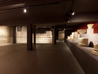 Ubiermonument Ein Museumsraum mit schummerigem Licht zeigt antike Steine und Säulenreste in einem kargen Keller.A museum room with dim lighting shows ancient stones and the remains of columns in a barren cellar.