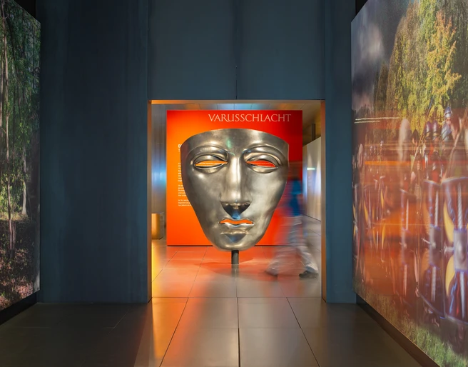 Varusschlacht im Osnabrücker Land - Museum und Park Kalkriese Große silberne Maske im Varusschlacht-Museum mit Besucher im Flur.