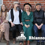6 Rhiannon.jpg Sechs Mitglieder der Fleetwood‑Mac‑Coverband Rhiannon sitzen entspannt vor einer Backsteinwand auf einer niedrigen Mauer, lachend oder lässig in die Kamera – darunter zwei Frauen und vier Männer – mit dem Schriftzug ‚Eisenhütte – Café · Restaurant · Kultur‘ und dem Bandnamen ‚Rhiannon‘.