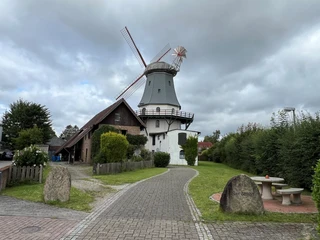 Windmühle Etelsen Historische Windmühle in Etelsen mit grüner Umgebung und benachbartem Backsteingebäude unter wolkigem Himmel.