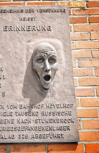 Gedenktafel am Hövelhof Bahnhof mit Relief eines schreienden Gesichts erinnert an Kriegsgefangene.