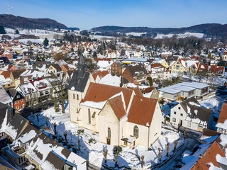 Luftaufnahme einer verschneiten Stadt mit einer großen Kirche im Zentrum, umgeben von schneebedeckten Häusern.