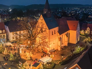 Luftaufnahme eines festlich beleuchteten Weihnachtsmarktes vor einer Kirche in einer abendlichen Szenerie.
