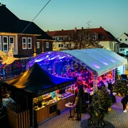 Gänseliesels Weihnachtslounge Weihnachtslounge mit glitzernden Lichtern, überdachten Marktständen und einem Weihnachtsengel in Monheim.