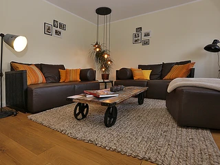 Soul Place Mahatma Gandhi  Ein Wohnzimmer mit braunen Sofas, orangefarbenen Kissen und einem Holztisch auf einem Teppich.
