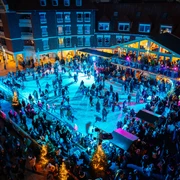 Der Monheimer Sternenzauber mit Eislaufbahn Blick auf eine belebte Eislaufbahn bei Nacht, umgeben von festlich beleuchteten Gebäuden und Bäumen.