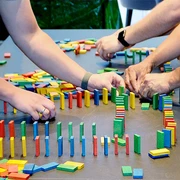 Drei Personen bauen ein Dominospiel auf mSa Team-Bash
