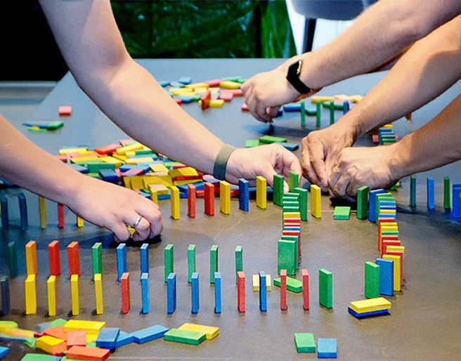 Three people are setting up a game of dominoes. mSa Team-Bash