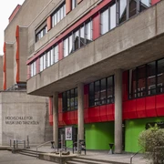 University of Music and Dance Markantes Gebäude der Hochschule für Musik und Tanz Köln mit roten und grünen Akzenten an der Fassade, umgeben von Bäumen und urbaner Architektur.Striking building of the Cologne University of Music and Dance with red and green accents on the façade, surrounded by trees and urban architecture.