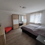 Moderner Schlafraum mit Doppelbett, großem Schrank, Nachttisch und rotem Sitzhocker, hell dekoriert.