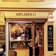 Hofladen15.jpg Fassade eines Hofladens bei Nacht, beleuchtet, mit Schaufenster voller Wurstwaren und Kreidetafeln mit handgeschriebenen Angeboten.