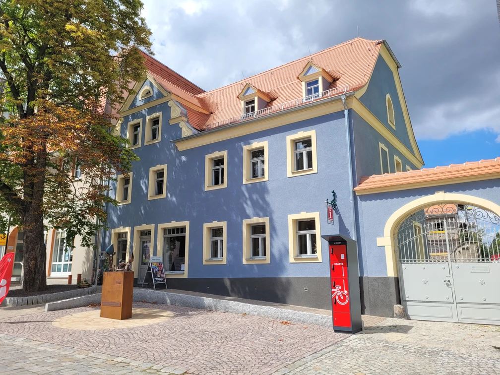 Tourist-Information Bad Lausick mit E-Bike Ladestation - Besucherberatung und Service Außenansicht der Touristinformation Bad Lausick, die Fassade ist leuchtend blau, auf der linken Seite des Eingangs steht eine Kastanie