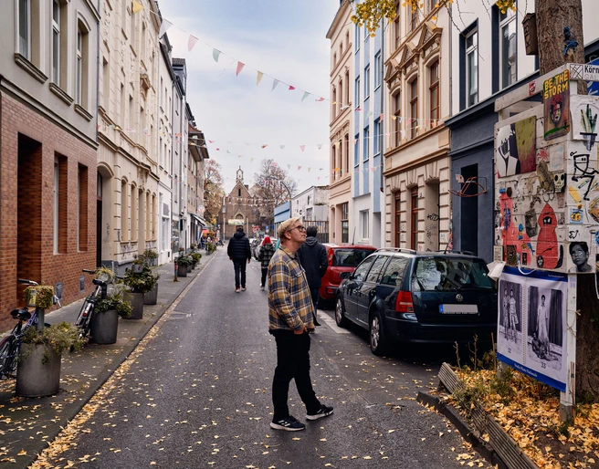 Körnerstraße  Körnerstraße in Köln-Ehrenfeld: Bunte Häuser, Kunstplakate an einem Baum, schlendernde Passant*innen.Körnerstraße in Cologne-Ehrenfeld: Colorful houses, art posters on a tree, strolling passers-by.