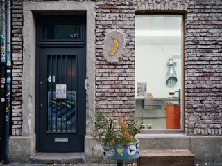 Körnerstraße  Backsteinfassade mit Glastür, Pflanzkübel und bananaförmiges Wandrelief.Brick façade with glass door, planter and banana-shaped wall relief.