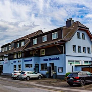 Haus Rheinblick Ott, Monheim am Rhein Dreistöckiges Gästehaus mit Parkmöglichkeiten, blau-weißer Fassade und Eifeler-Landbier-Schild.