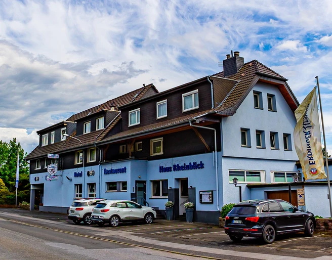 Haus Rheinblick Ott, Monheim am Rhein Dreistöckiges Gästehaus mit Parkmöglichkeiten, blau-weißer Fassade und Eifeler-Landbier-Schild.