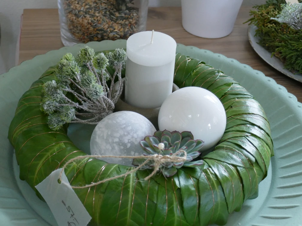 Adventsgesteck Ein dekorativer Adventskranz aus grünen Blättern mit Kerze, weißen Kugeln und einer Sukkulente.