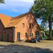 Rotes Backsteinhaus unter strahlend blauem Himmel, mit parkendem schwarzen Auto auf der Einfahrt.