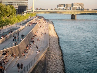 Rheinboulevard Das Bild zeigt den Rheinboulevard in Köln bei gutem Wetter. Menschen sitzen auf breiten Stufen am Flussufer und genießen die Aussicht auf den Rhein. The picture shows the Rheinboulevard in Cologne in good weather. People sit on wide steps on the riverbank and enjoy the view of the Rhine.