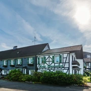Außenansicht von Lohmanns Romantik Hotel Gravenberg in Langenfeld Fachwerkgebäude von Lohmanns Romantik Hotel Gravenberg in Langenfeld mit grünen Akzenten unter blauem Himmel.