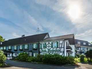 Außenansicht von Lohmanns Romantik Hotel Gravenberg in Langenfeld Fachwerkgebäude von Lohmanns Romantik Hotel Gravenberg in Langenfeld mit grünen Akzenten unter blauem Himmel.
