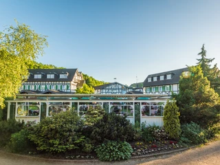 Lohmanns Romantik Hotel Gravenberg in Langenfeld Ein elegantes Fachwerkhotel umgeben von üppigem Grün unter strahlend blauem Himmel.