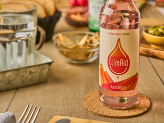 ClimAid Limonade Rhabarber ClimAid Limonade in Rhabarber-Geschmack steht auf einem Tisch neben Schalen und einem Glas Wasser.