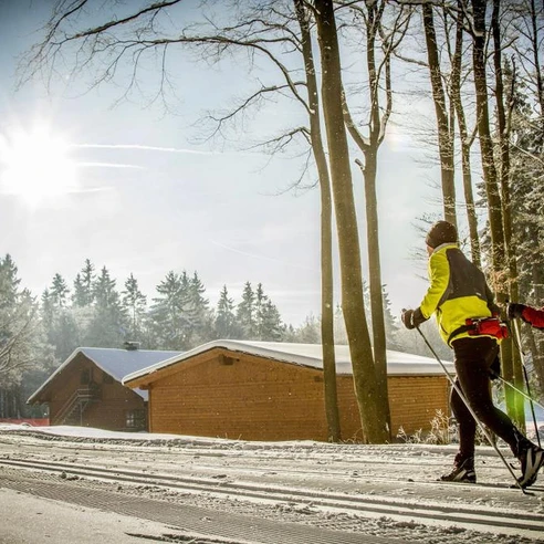 Langläufer in der Loipe vor Holzhütten  Langläufer in der Loipe vor Holzhütten