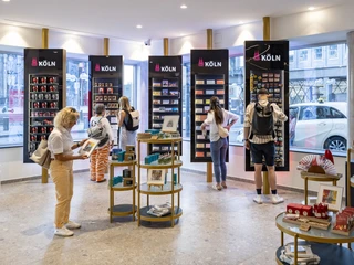 Tourist Information Cologne Innenansicht der Kölner Touristeninformation mit Besuchern, die Souvenirs durchstöbern.Interior view of the Cologne tourist information office with visitors browsing through souvenirs.