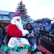 Weihnachtsmann mit Kutsche Weihnachtsmann in rotem Mantel auf Kutsche verteilt Süßigkeiten an Kinder auf festlichem Markt.