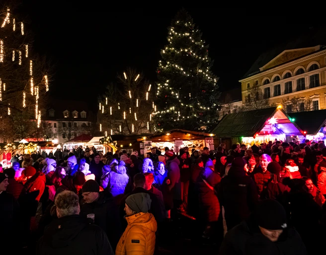 Delitzscher Adventsmarkt Marktplatz Zusehen ist eine Menschengruppe am Abend auf dem Delitzscher Marktplatz. Im Hintergrund sind beleuchtete Nadelbäume und weihnachliche Stände.