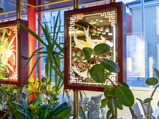 Wan Bao Wan Bao Fensterdekoration mit leuchtenden Bildern von Fischen und Blumen. Darum viele Zimmerpflanzen.