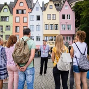 Guided tour of the fish market in Cologne's old town Eine Gruppe von Menschen steht am historischen Fischmarkt in Köln. Im Hintergrund sind bunte Fachwerkhäuser zu sehen, die eine lebendige und einladende Kulisse bilden.A group of people stand at the historic fish market in Cologne. Colorful half-timbered houses can be seen in the background, creating a lively and inviting backdrop.