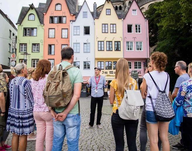 Guided tour of the fish market in Cologne's old town Eine Gruppe von Menschen steht am historischen Fischmarkt in Köln. Im Hintergrund sind bunte Fachwerkhäuser zu sehen, die eine lebendige und einladende Kulisse bilden.A group of people stand at the historic fish market in Cologne. Colorful half-timbered houses can be seen in the background, creating a lively and inviting backdrop.