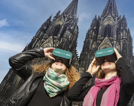 TimeRide VR-Domtour Zwei Personen genießen mit VR-Brillen vor dem Kölner Dom eine immersive Tour.Two people enjoy an immersive tour with VR glasses in front of Cologne Cathedral.